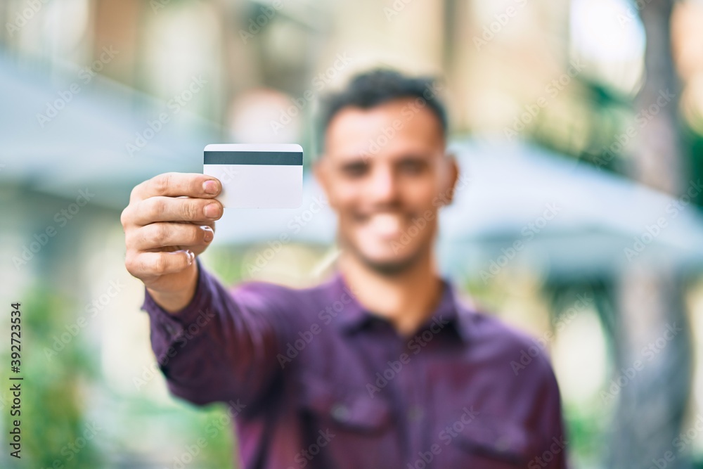 Young hispanic man smiling happy holding credit card at the city. Young hispanic man smiling happy holding credit card at the city.