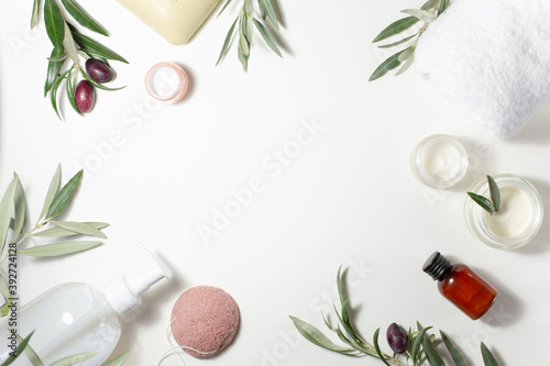 Spa and beauty. A set of natural cosmetics. Soap, cream, white towel, sponge and olive tree sprigs are arranged around the perimeter on a white background. Copy space.