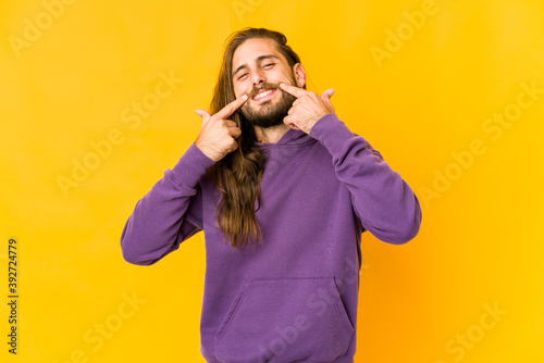 Young man with long hair look smiles  pointing fingers at mouth.