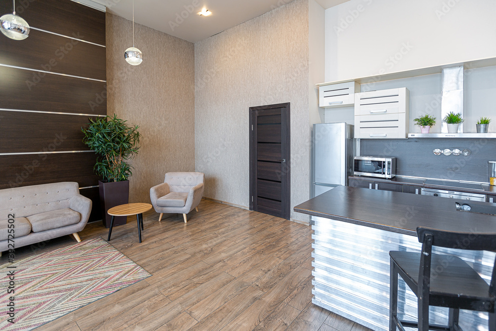 Fototapeta premium Contemporary ordinary design of spacious studio in soft warm colors. Simple furniture. Light large room with sunlight. Daytime. Tiled brown floor and white walls .