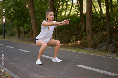 Woman runner stretching legs before exercising summer park morning