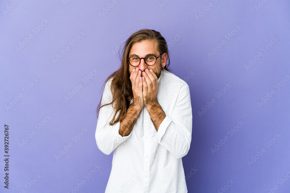 Young man with long hair look laughing about something, covering mouth with hands.