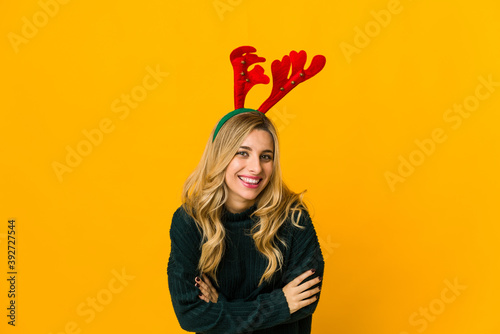 Young blonde caucasian woman wearing reindeer horns laughing and having fun. © Asier