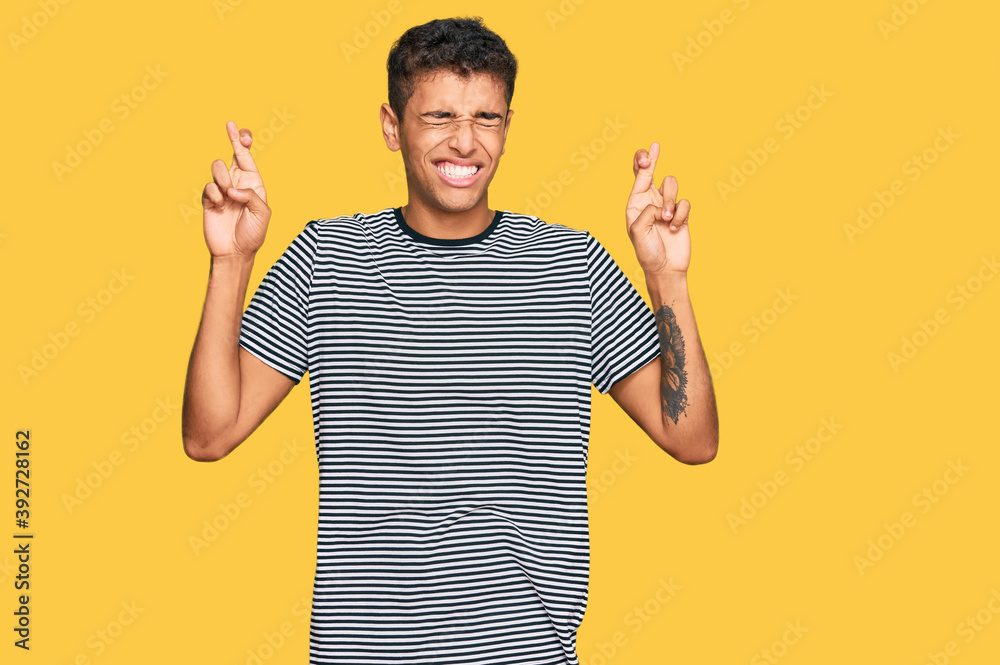 Young handsome african american man wearing casual clothes gesturing finger crossed smiling with hope and eyes closed. luck and superstitious concept.
