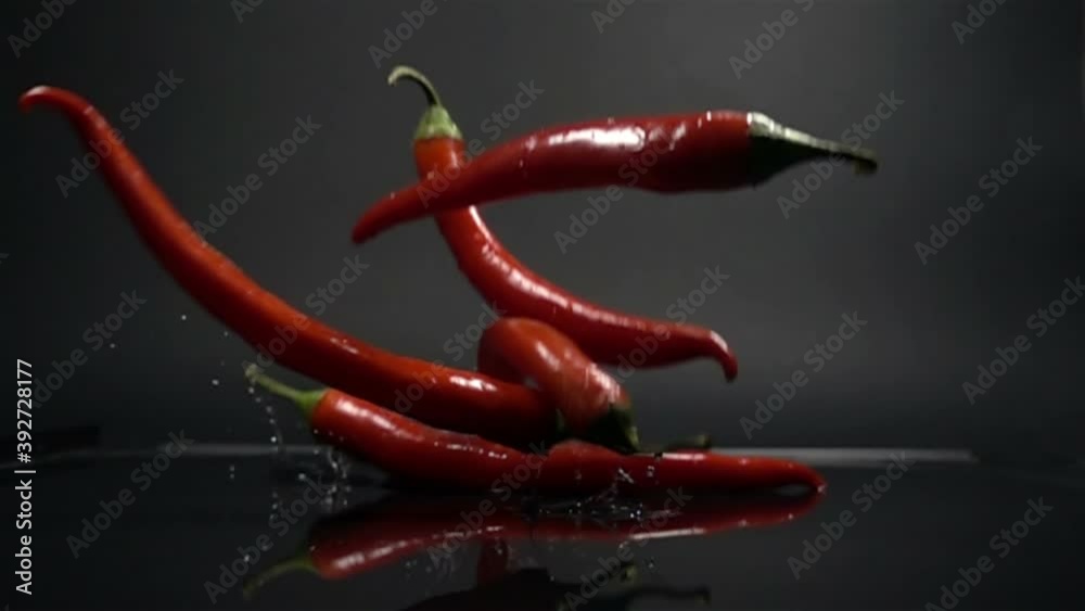 Red Chili Peppers falling into the water in slow motion on black background