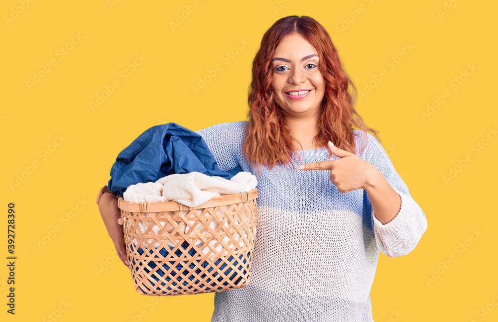 Young latin woman holding laundry basket smiling happy pointing with hand and finger Young latin woman holding laundry basket smiling happy pointing with hand and finger