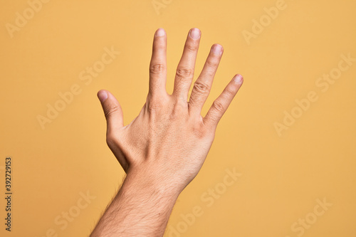 Hand of caucasian young man showing fingers over isolated yellow background counting number 5 showing five fingers