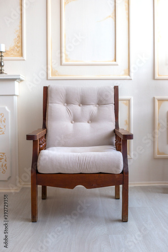 Wooden armchair with a soft white seat stands on the antique beige wall background