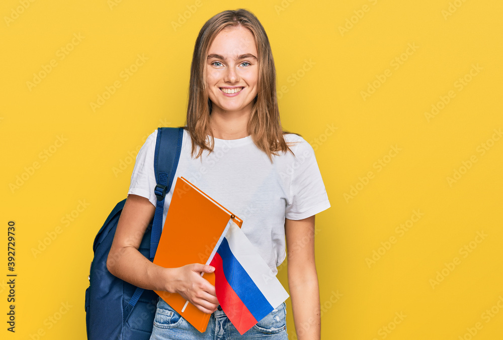 Beautiful young blonde woman exchange student holding russian flag looking positive and happy standing and smiling with a confident smile showing teeth Beautiful young blonde woman exchange student holding russian flag looking positive and happy standing and smiling with a confident smile showing teeth