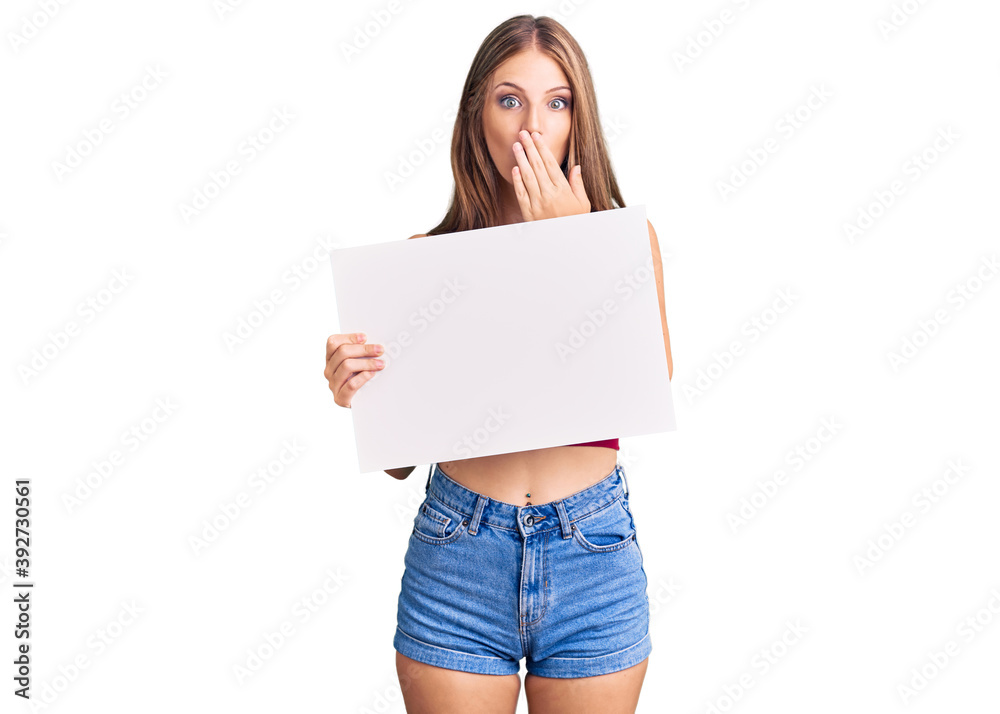Young beautiful blonde woman holding blank empty banner covering mouth with hand, shocked and afraid for mistake. surprised expression Young beautiful blonde woman holding blank empty banner covering mouth with hand, shocked and afraid for mistake. surprised expression