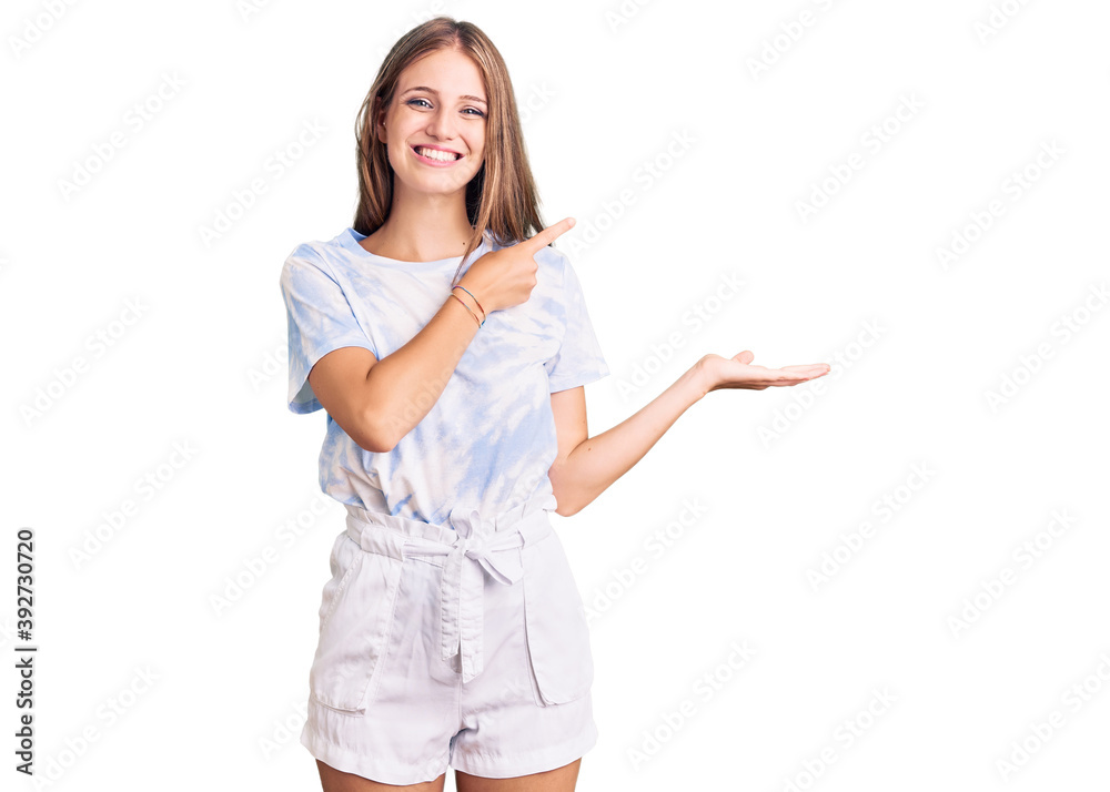 Young beautiful blonde woman wearing tye die tshirt amazed and smiling to the camera while presenting with hand and pointing with finger. Young beautiful blonde woman wearing tye die tshirt amazed and smiling to the camera while presenting with hand and pointing with finger.