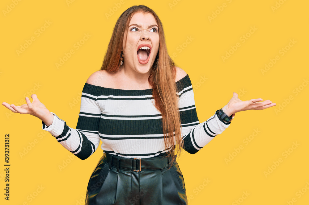 Young beautiful redhead woman wearing elegant clothes crazy and mad shouting and yelling with aggressive expression and arms raised. frustration concept. Young beautiful redhead woman wearing elegant clothes crazy and mad shouting and yelling with aggressive expression and arms raised. frustration concept.