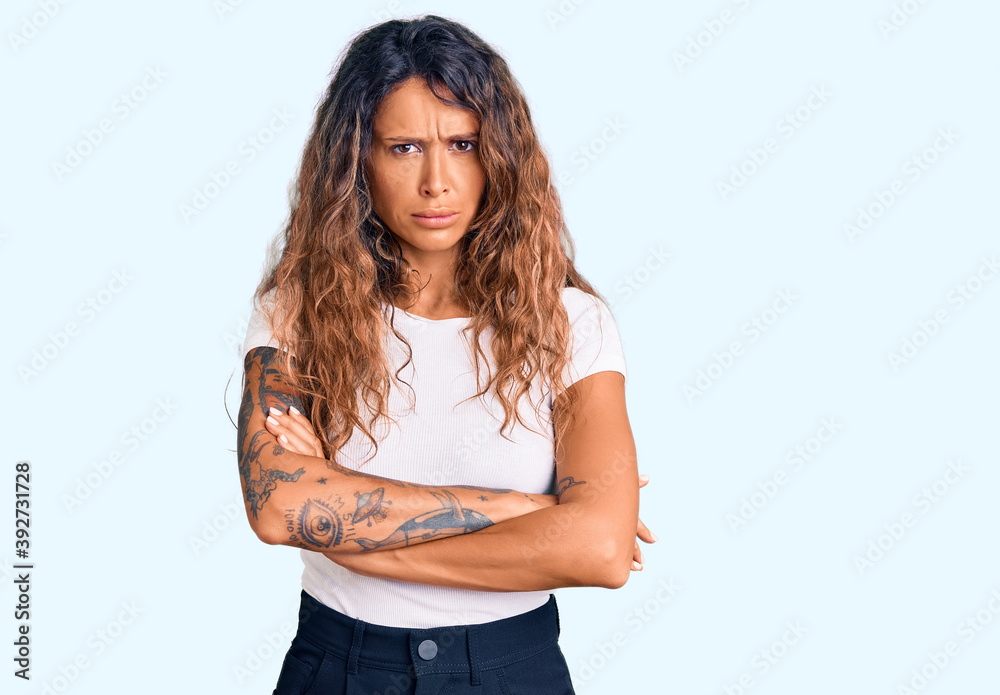 Young hispanic woman with tattoo wearing casual white tshirt skeptic and nervous, disapproving expression on face with crossed arms. negative person. Young hispanic woman with tattoo wearing casual white tshirt skeptic and nervous, disapproving expression on face with crossed arms. negative person.
