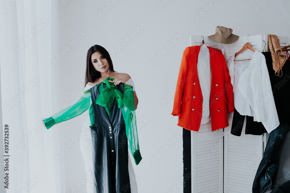 Woman choosing outfit from large wardrobe closet with stylish clothes and home stuff