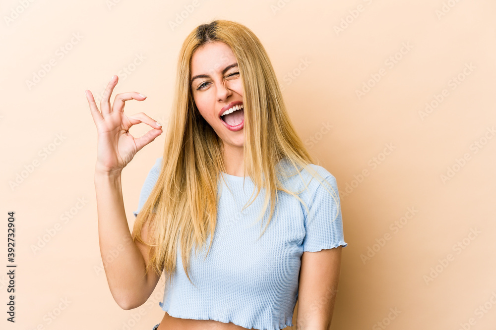 Young blonde caucasian woman winks an eye and holds an okay gesture with hand. Young blonde caucasian woman winks an eye and holds an okay gesture with hand.
