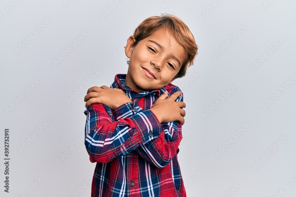 Adorable latin kid wearing casual clothes hugging oneself happy and positive, smiling confident. self love and self care Adorable latin kid wearing casual clothes hugging oneself happy and positive, smiling confident. self love and self care