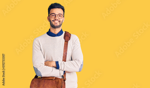 Young handsome hispanic man wearing leather bag happy face smiling with crossed arms looking at the camera. positive person.