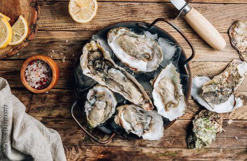 Fresh oysters with ice and lemon on a rustic wooden background.