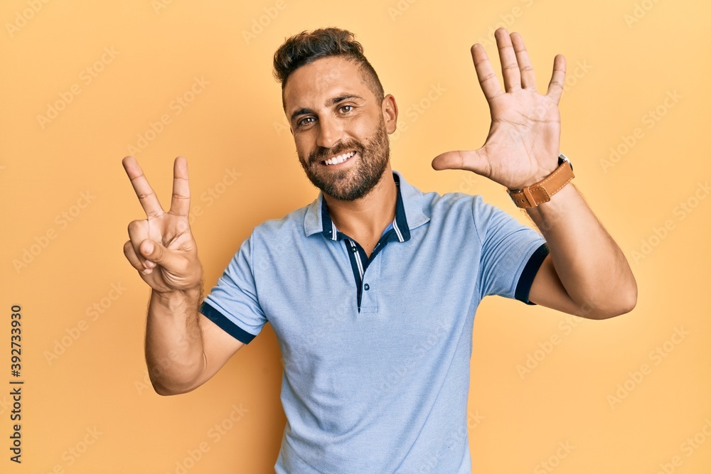 Fototapeta premium Handsome man with beard wearing casual clothes showing and pointing up with fingers number seven while smiling confident and happy.