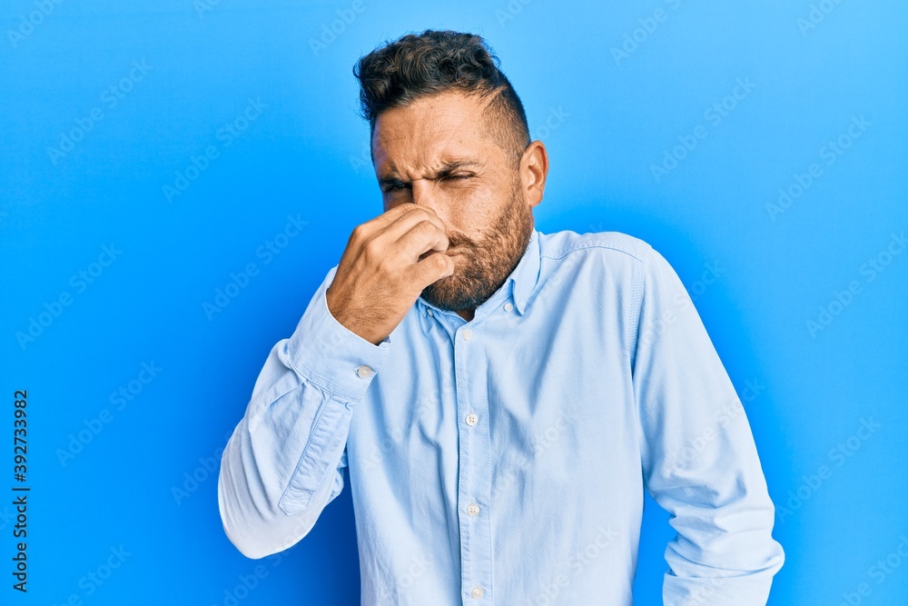 Handsome man with beard wearing casual clothes smelling something stinky and disgusting, intolerable smell, holding breath with fingers on nose. bad smell Handsome man with beard wearing casual clothes smelling something stinky and disgusting, intolerable smell, holding breath with fingers on nose. bad smell