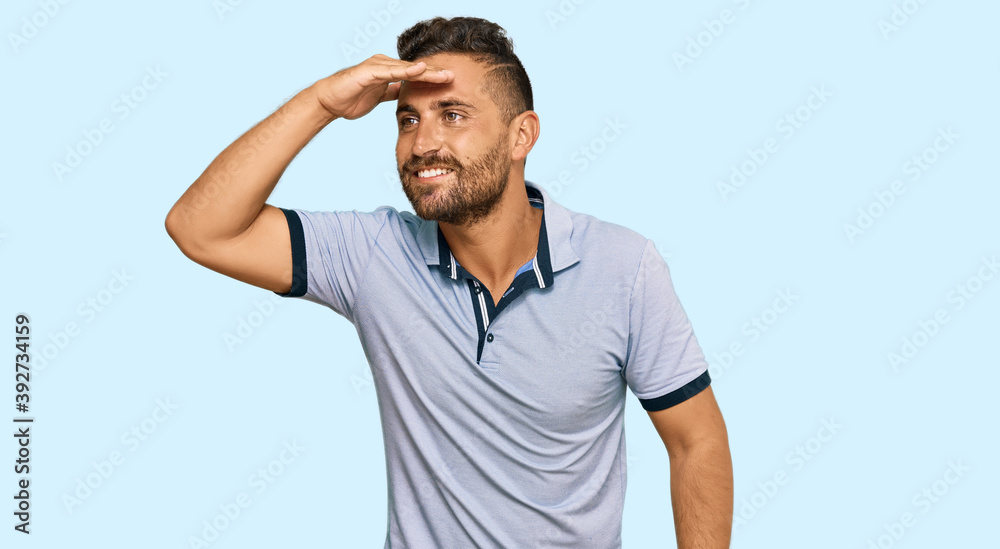 Handsome man with beard wearing casual clothes very happy and smiling looking far away with hand over head. searching concept. Handsome man with beard wearing casual clothes very happy and smiling looking far away with hand over head. searching concept.