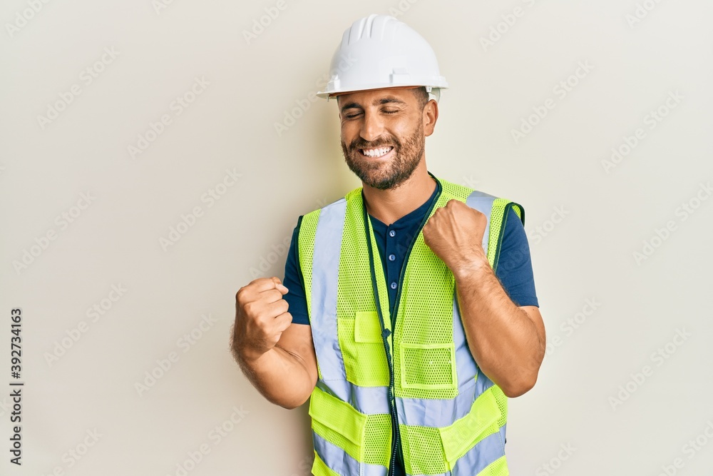 Handsome man with beard wearing safety helmet and reflective jacket celebrating surprised and amazed for success with arms raised and eyes closed Handsome man with beard wearing safety helmet and reflective jacket celebrating surprised and amazed for success with arms raised and eyes closed