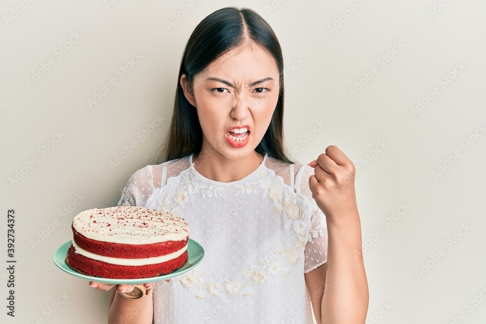 Young chinese woman holding carrot cake annoyed and frustrated shouting with anger, yelling crazy with anger and hand raised Young chinese woman holding carrot cake annoyed and frustrated shouting with anger, yelling crazy with anger and hand raised