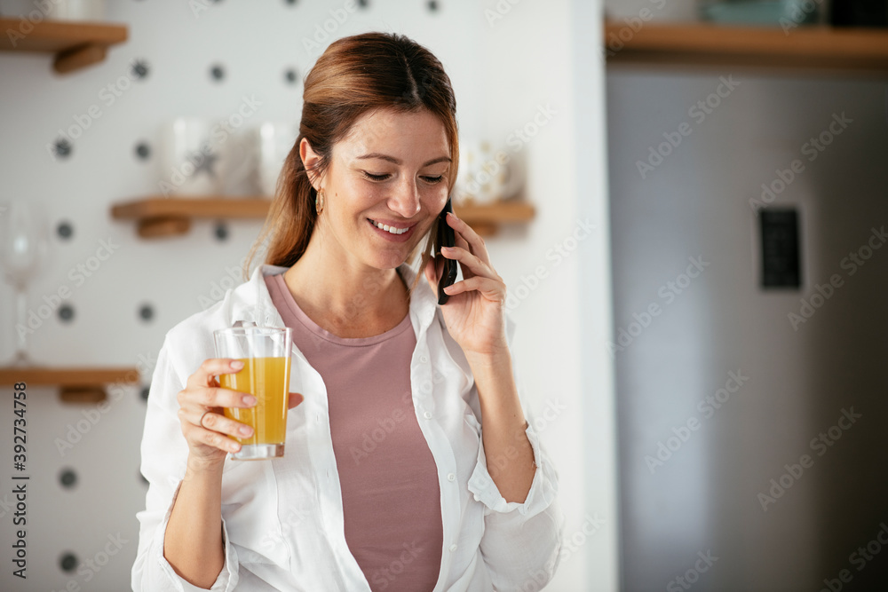 Young woman in kitchen. Beautiful woman preparing breakfast and using the phone.