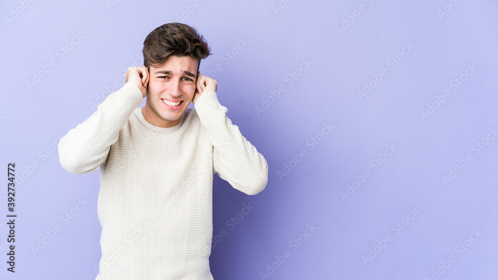 Young caucasian man isolated on purple background covering ears with hands. Young caucasian man isolated on purple background covering ears with hands.