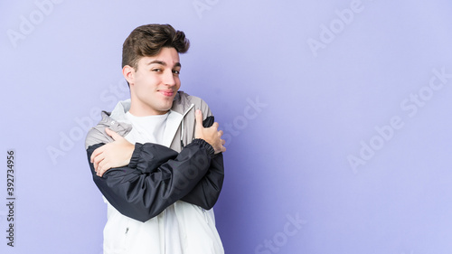 Young caucasian man isolated on purple background hugs, smiling carefree and happy.