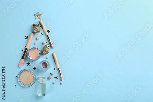 Christmas tree shape of decorative cosmetic products on light blue background, flat lay with space for text. Winter care