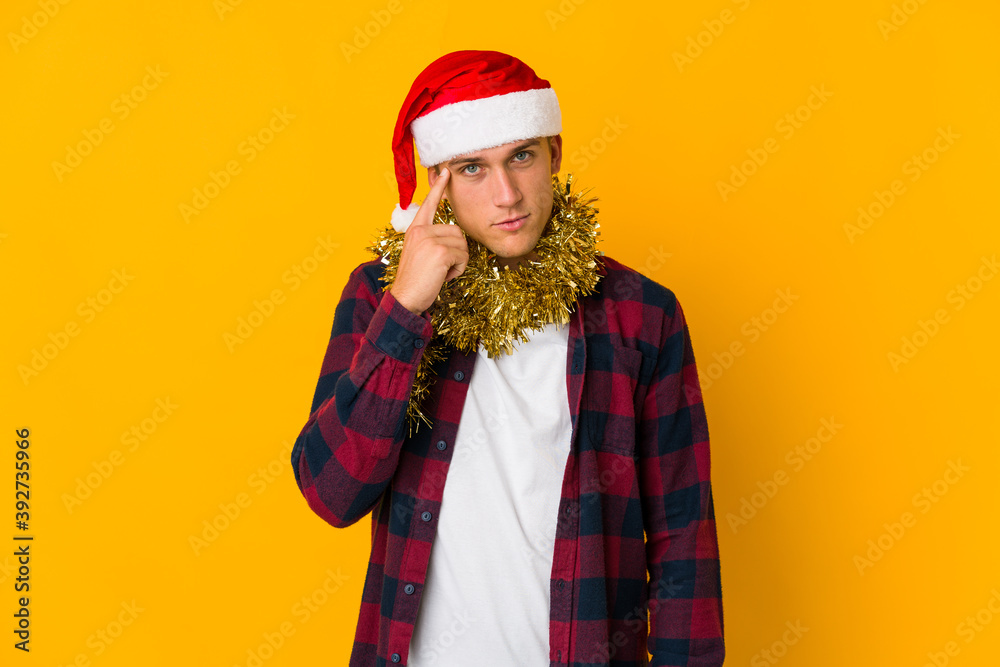 Young caucasian man with christmas hat holding a present isolated on yellow background Young caucasian man with christmas hat holding a present isolated on yellow background