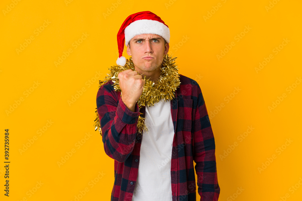 Young caucasian man with christmas hat holding a present isolated on yellow background Young caucasian man with christmas hat holding a present isolated on yellow background