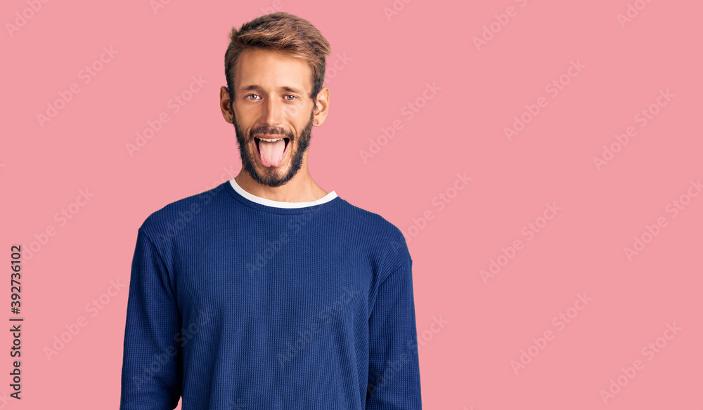 Handsome blond man with beard wearing casual sweater sticking tongue out happy with funny expression. emotion concept. Handsome blond man with beard wearing casual sweater sticking tongue out happy with funny expression. emotion concept.