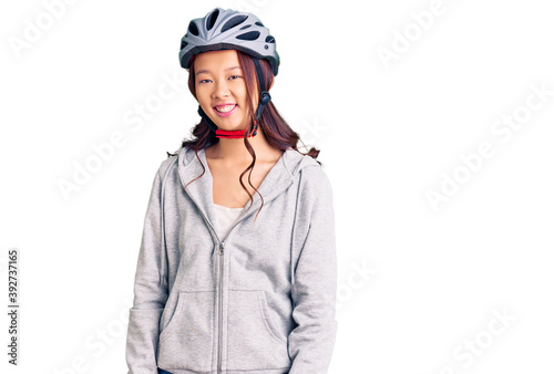 Young beautiful chinese girl wearing bike helmet looking positive and happy standing and smiling with a confident smile showing teeth © Krakenimages.com