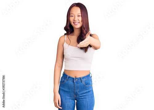 Young beautiful chinese girl wearing casual clothes smiling friendly offering handshake as greeting and welcoming. successful business.