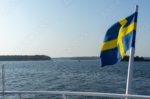 View of Swedish flag on boat rail. Stockholm archipelago in the background. Stockholm, Sweden