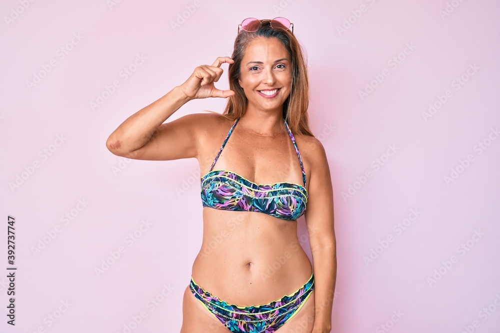 Naklejka premium Middle age hispanic woman wearing bikini smiling and confident gesturing with hand doing small size sign with fingers looking and the camera. measure concept.
