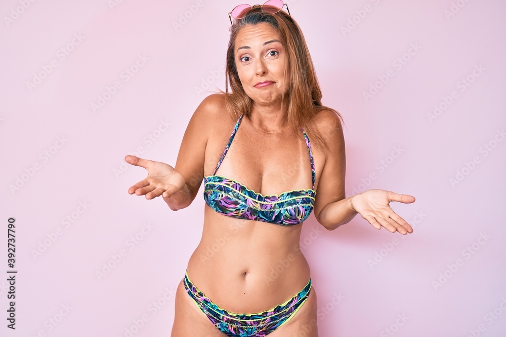 Middle age hispanic woman wearing bikini clueless and confused expression  with arms and hands raised. doubt concept. Photos | Adobe Stock