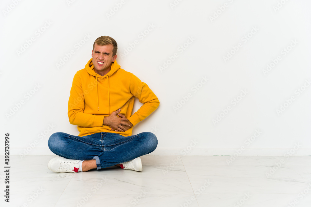 Young caucasian man sitting on the floor having a liver pain, stomach ache.