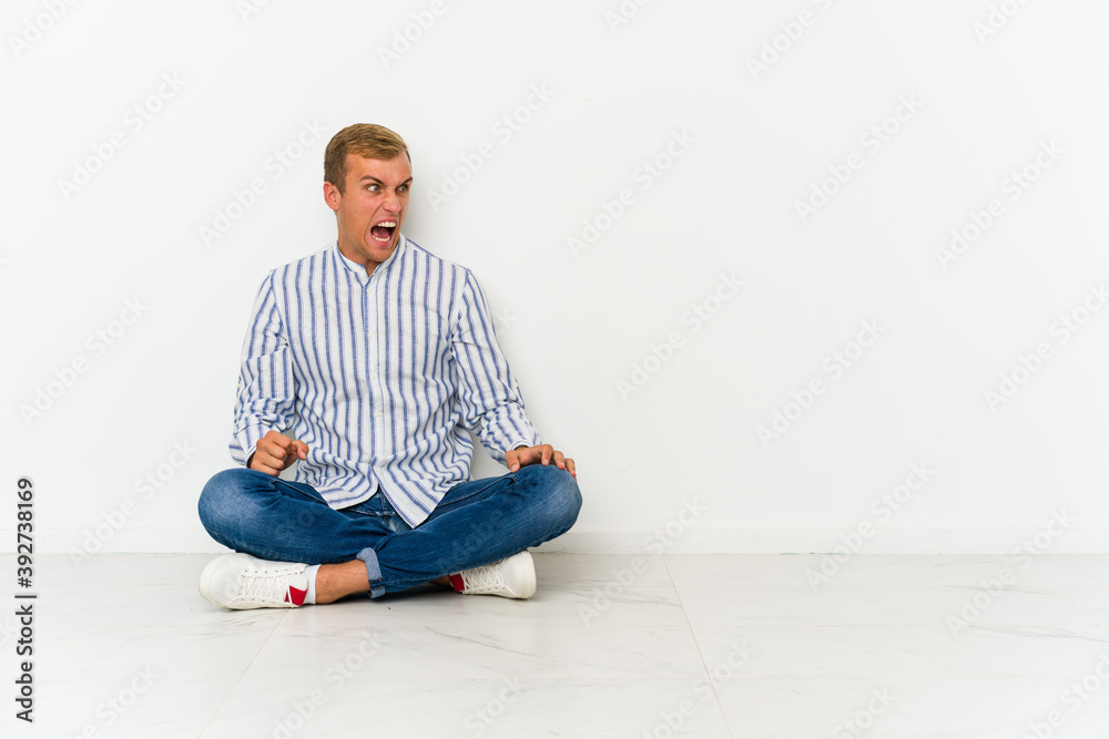 Young caucasian man sitting on the floor shouting very angry, rage concept, frustrated. Young caucasian man sitting on the floor shouting very angry, rage concept, frustrated.