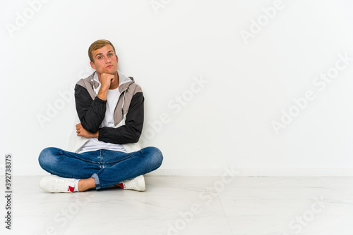 Young caucasian man sitting on the floor suspicious, uncertain, examining you.