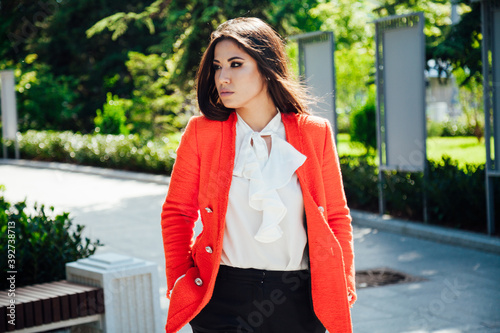 Beautiful brunette woman in red jacket on the street in the park