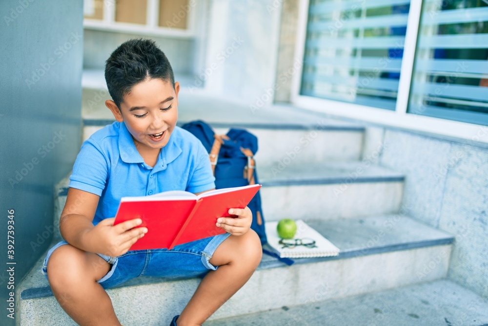 Adorable student boy reading book sitting on the stairs at school. Adorable student boy reading book sitting on the stairs at school.