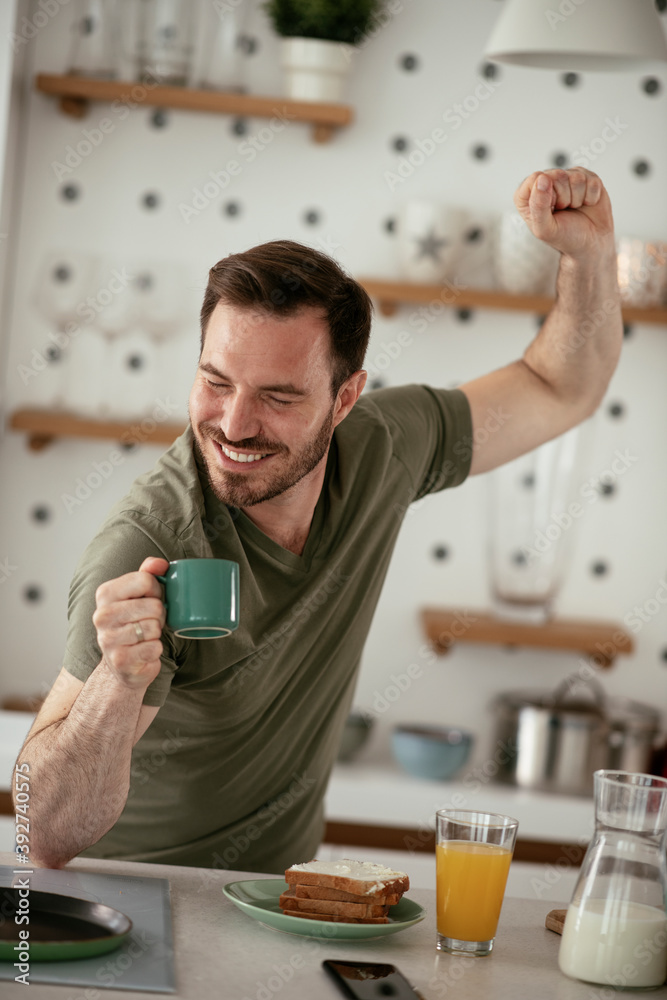 Handsome man preparing breakfast at home. Young man drinking coffee while preparing sandwich. Handsome man preparing breakfast at home. Young man drinking coffee while preparing sandwich.