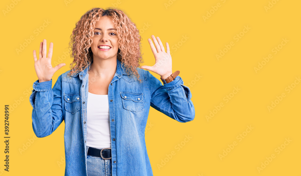 Young blonde woman with curly hair wearing casual denim jacket showing and pointing up with fingers number ten while smiling confident and happy.