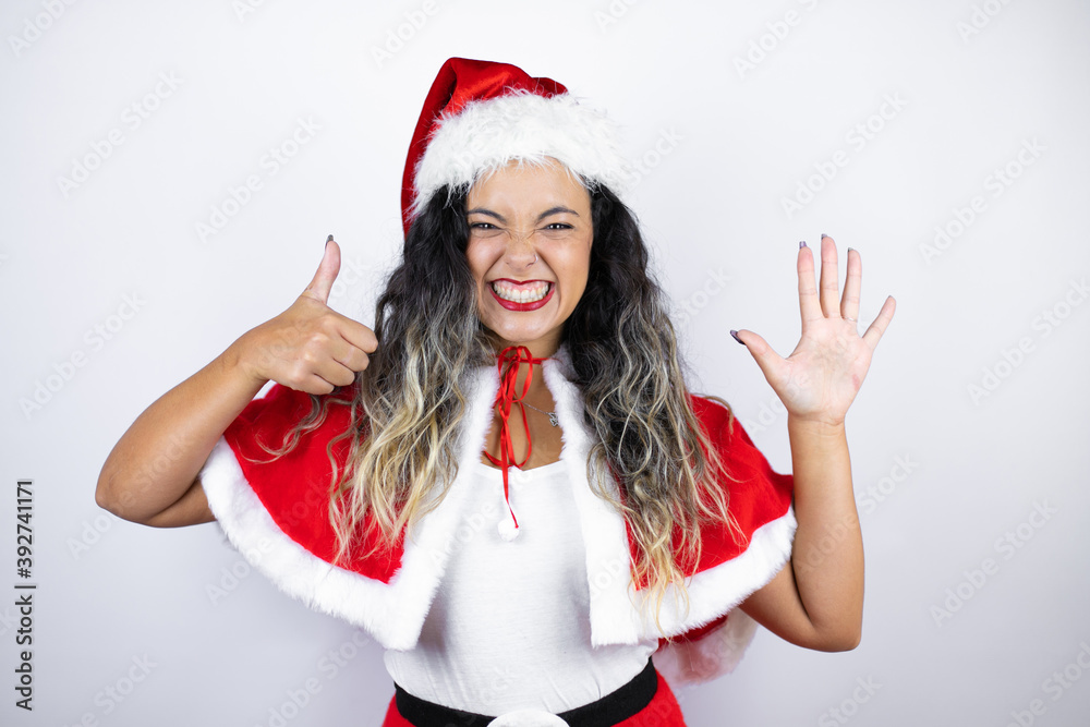 Young beautiful woman wearing a Santa Claus costume over white background showing and pointing up with fingers number six while smiling confident and happy Young beautiful woman wearing a Santa Claus costume over white background showing and pointing up with fingers number six while smiling confident and happy