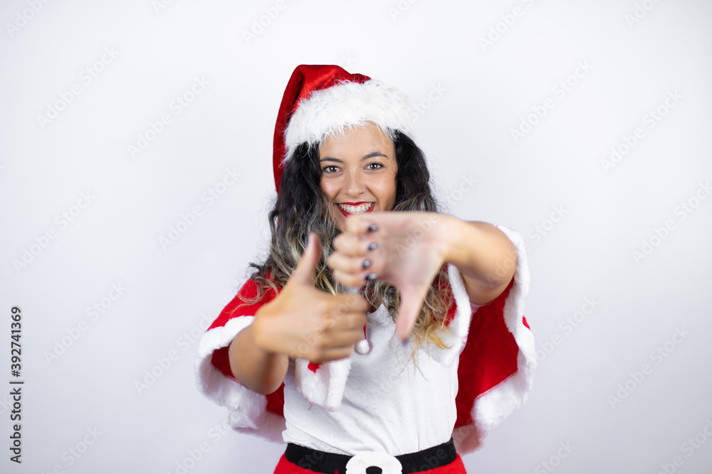 Obraz premium Young beautiful woman wearing a Santa Claus costume over white background Doing thumbs up and down, disagreement and agreement expression. Crazy conflict