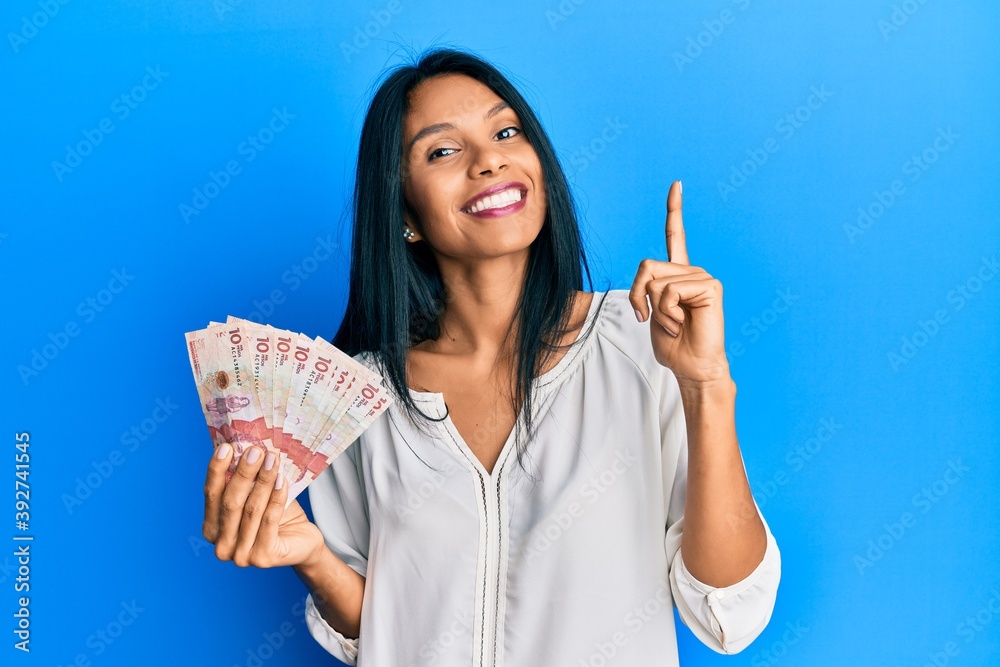 Young african american woman holding 10 colombian pesos banknotes pointing finger up with successful idea. exited and happy. number one. Young african american woman holding 10 colombian pesos banknotes pointing finger up with successful idea. exited and happy. number one.