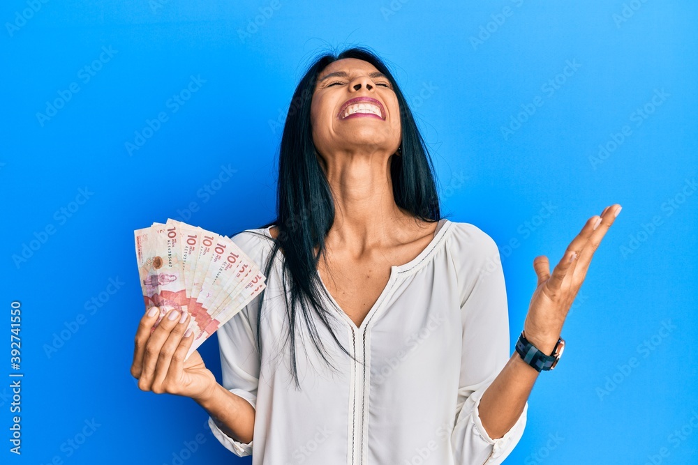 Young african american woman holding 10 colombian pesos banknotes crazy and mad shouting and yelling with aggressive expression and arms raised. frustration concept. Young african american woman holding 10 colombian pesos banknotes crazy and mad shouting and yelling with aggressive expression and arms raised. frustration concept.
